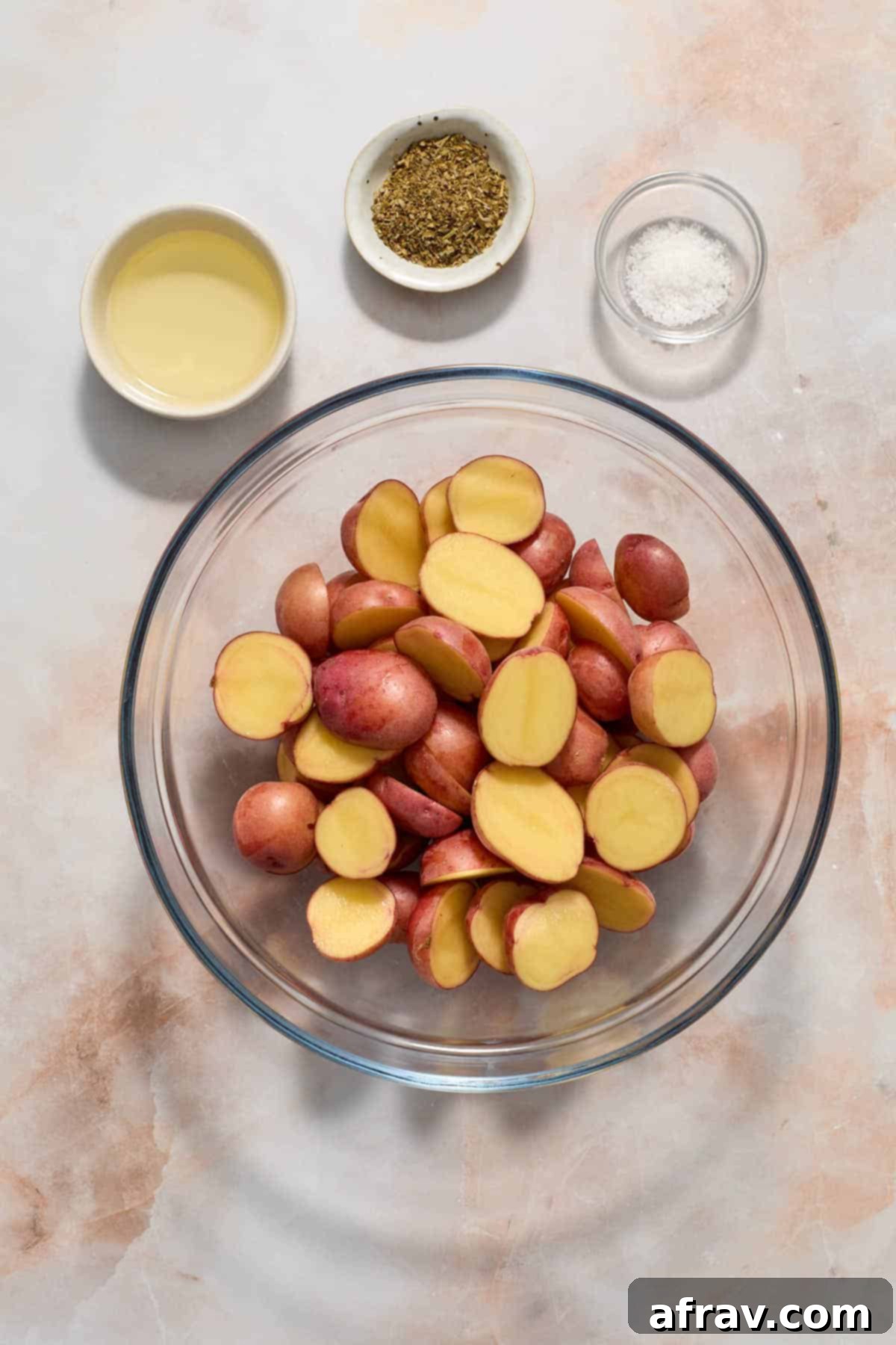 Potatoes cut in half and placed in a glass bowl with oil, seasonings and salt on the side.