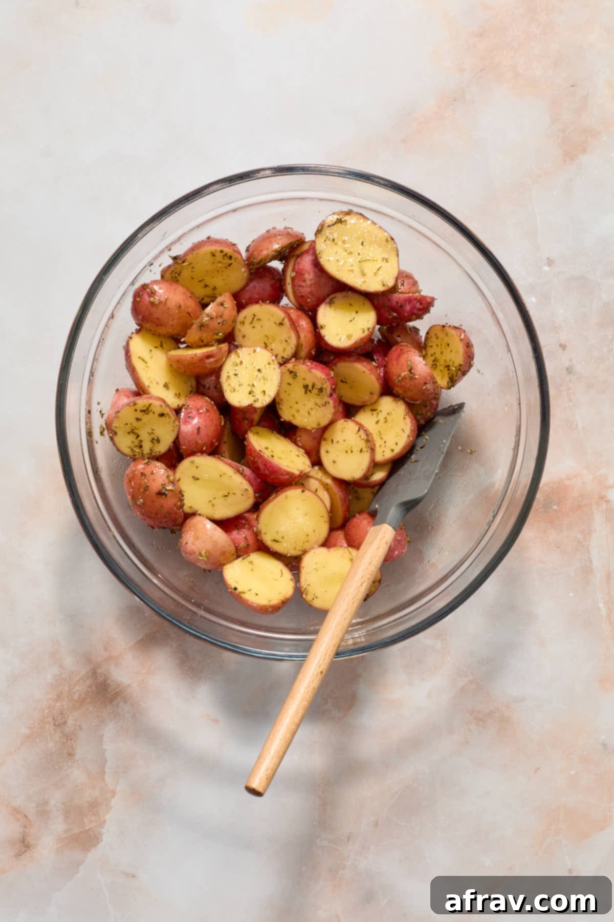 Seasoned potatoes mixed together in a bowl with a spatula.