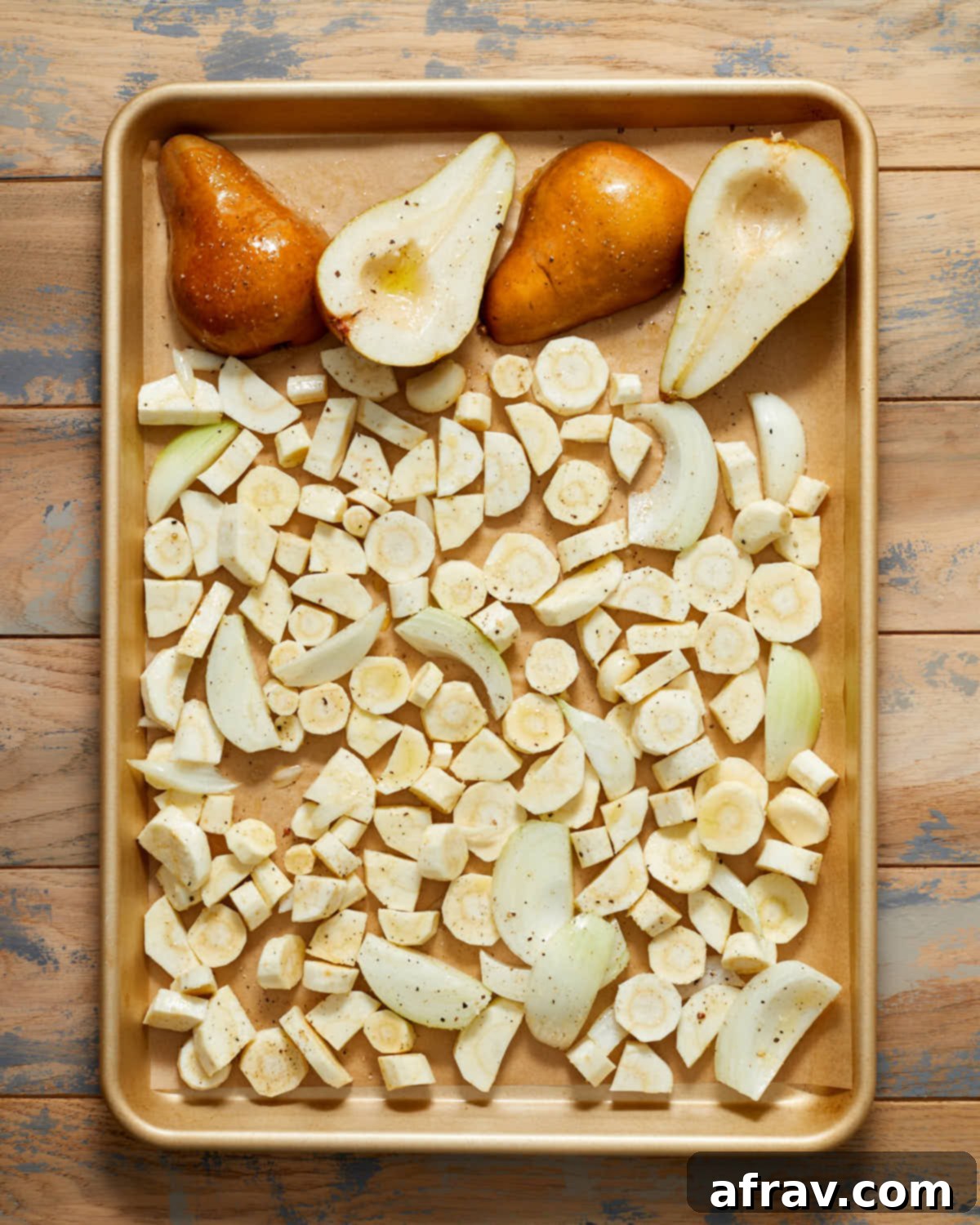 Chopped parsnip, pear halves, sliced onions and garlic arranged in single layer on a baking sheet.