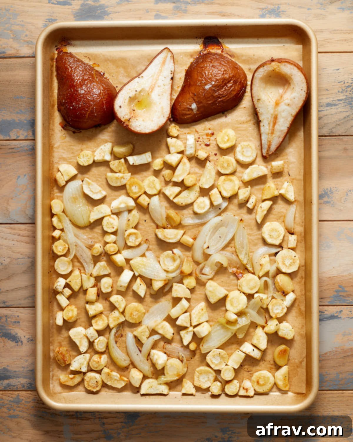 Roasted parsnips, pears, garlic and onions on a baking sheet.