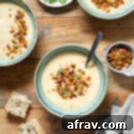 Parsnip and pear soup served in green bowls on a wooden table with savoury granola on top of the soup.