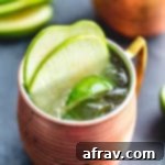 Green Apple Irish Mule in a copper mug and garnished with apple slices and lime wedges.