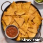 Air fryer tortilla chips served on a round platter with salsa and guacamole on the side.