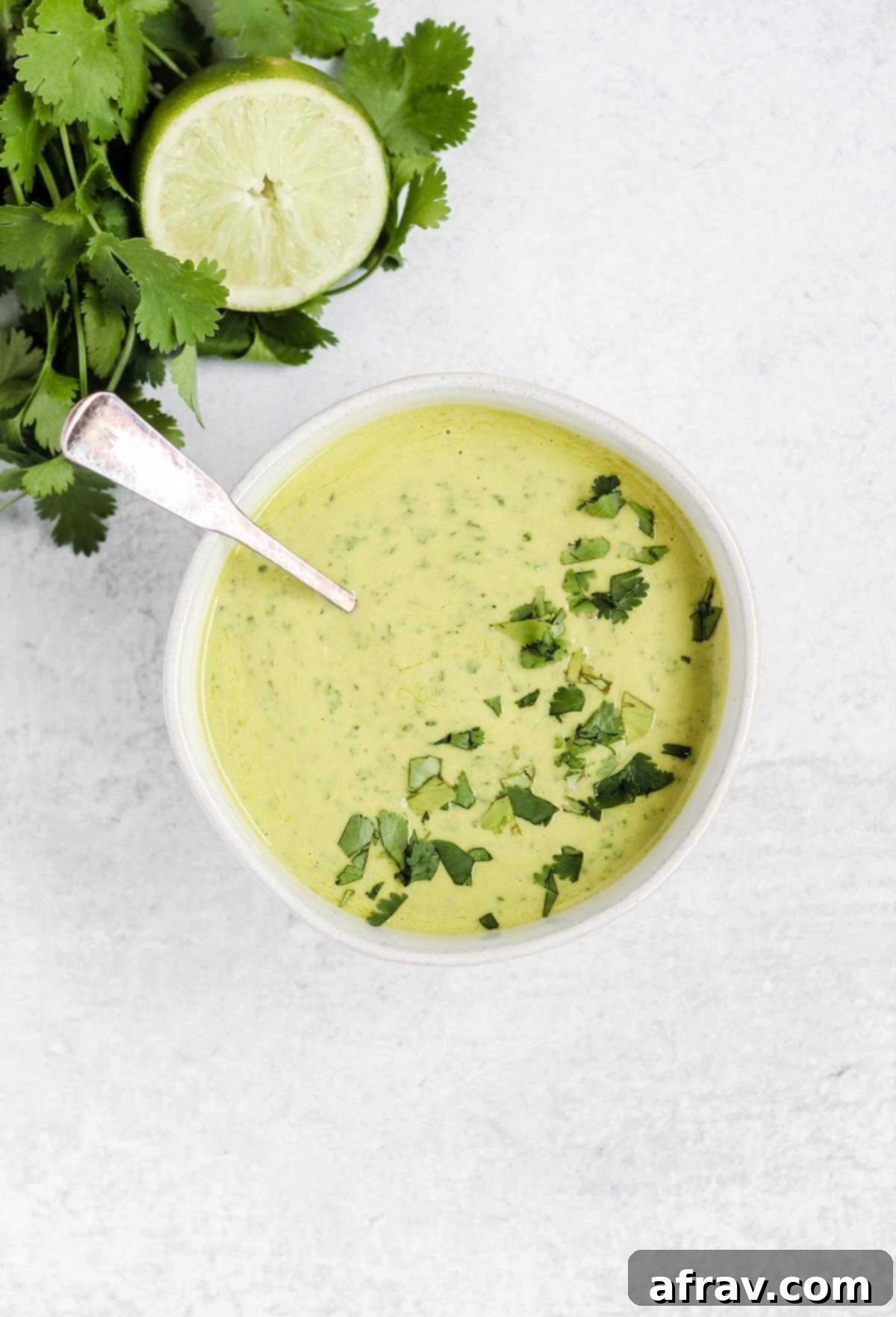 spoon dipping into a white bowl filled with creamy cilantro lime dressing