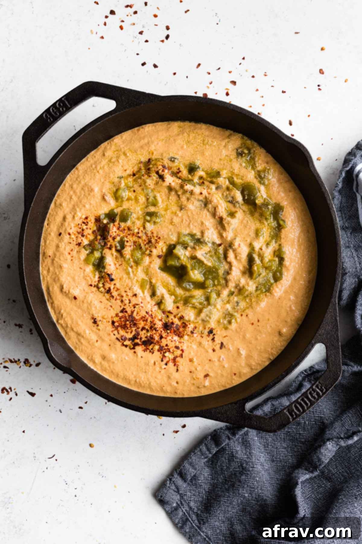 Overhead view of vegan queso in a black cast iron skillet with green chilis and red pepper flakes on top, ready for serving.