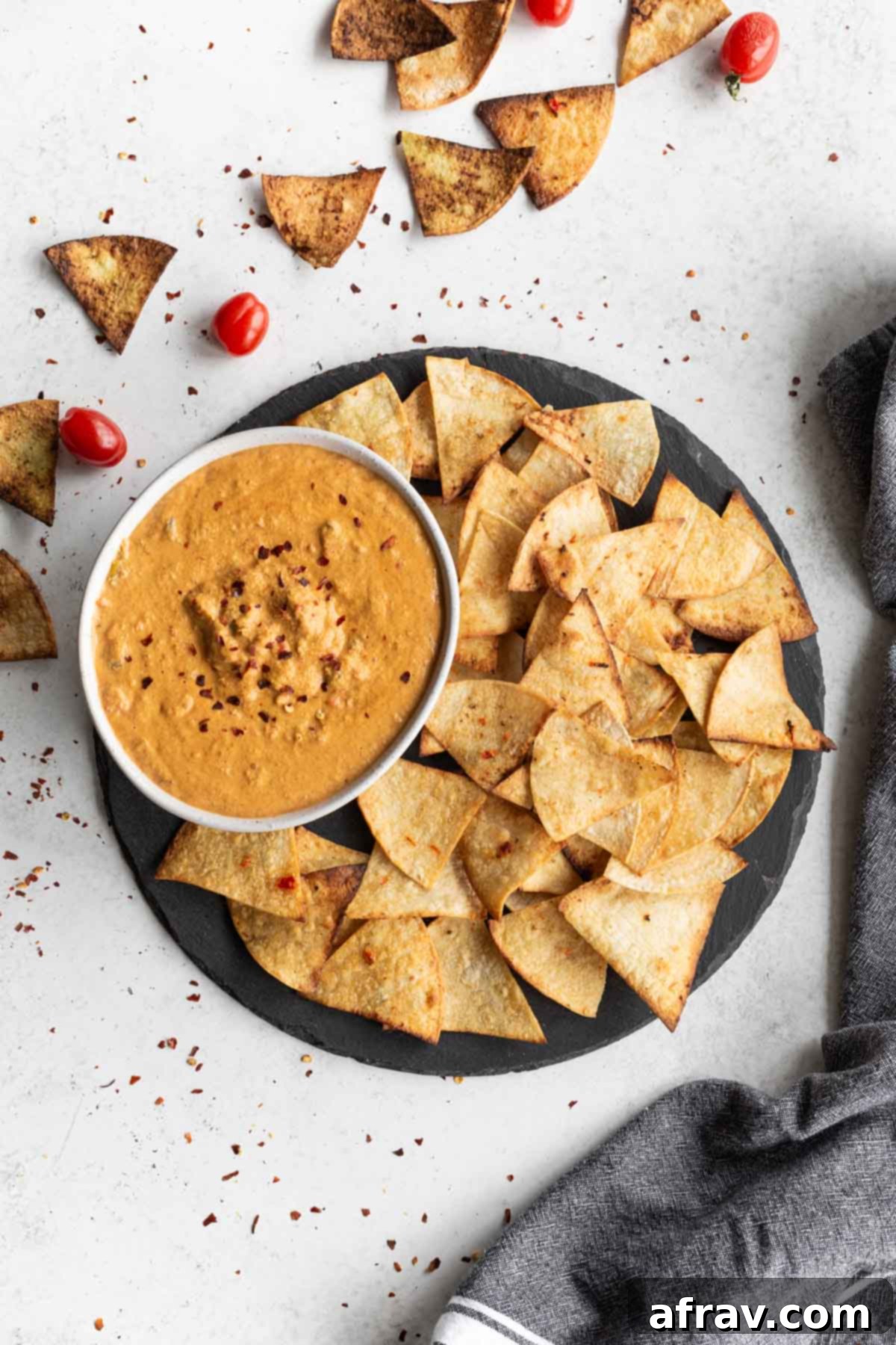 A bowl of creamy cashew queso, garnished with fresh herbs, served alongside tortilla chips on a rustic slate platter.