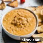 Up close view of cashew queso in a white bowl surrounded by tortilla chips, ready for dipping.