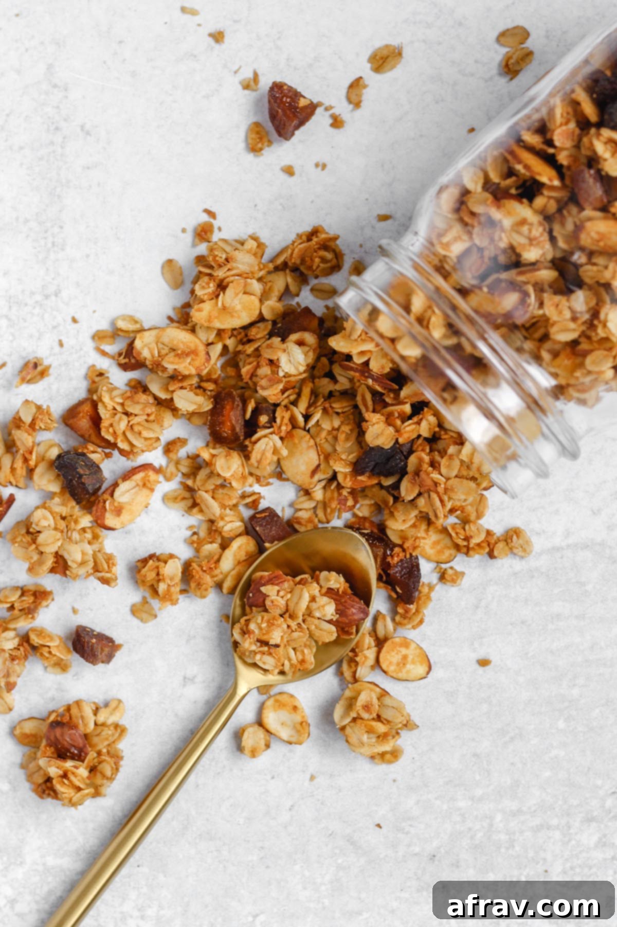 Golden brown homemade oat and honey granola spilling out of a mason jar, showcasing its delicious texture and inviting clusters.