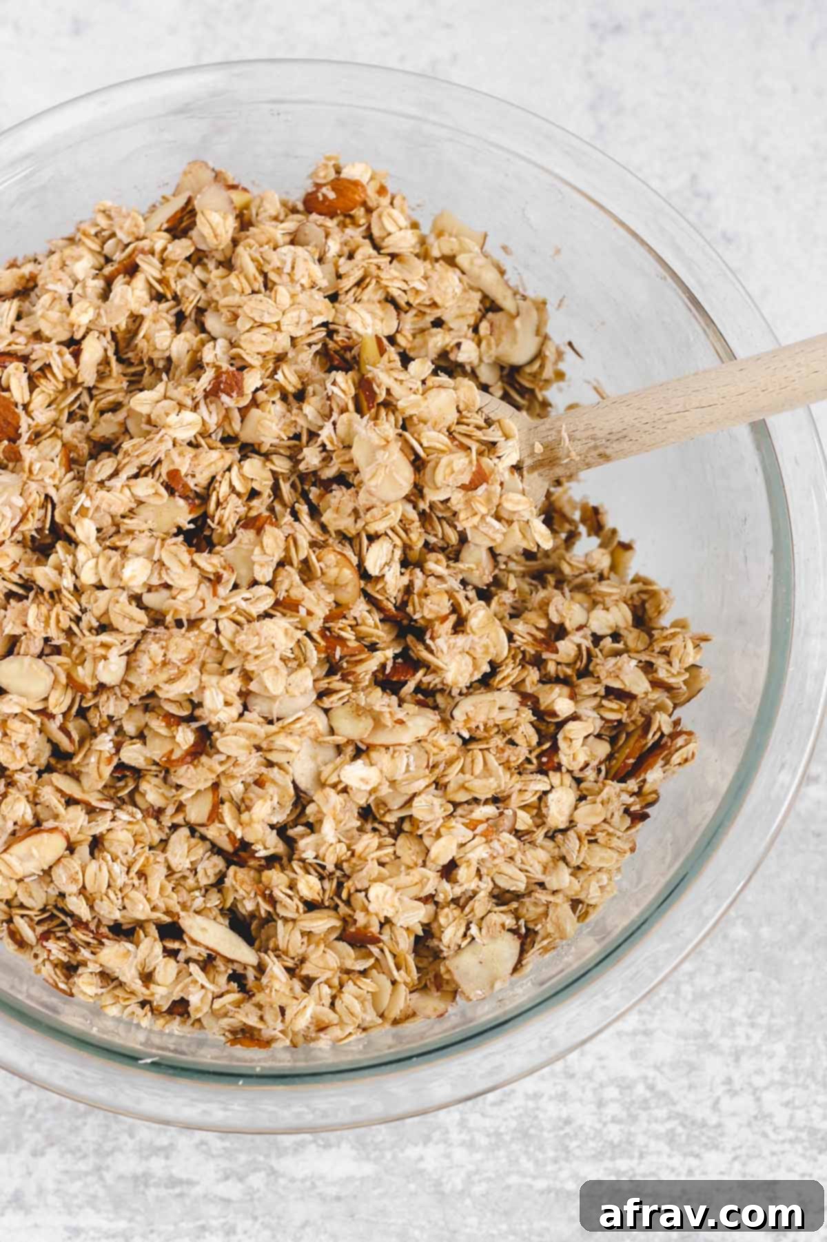 All oat and honey granola ingredients mixed together in a glass mixing bowl, fully coated and ready for baking.