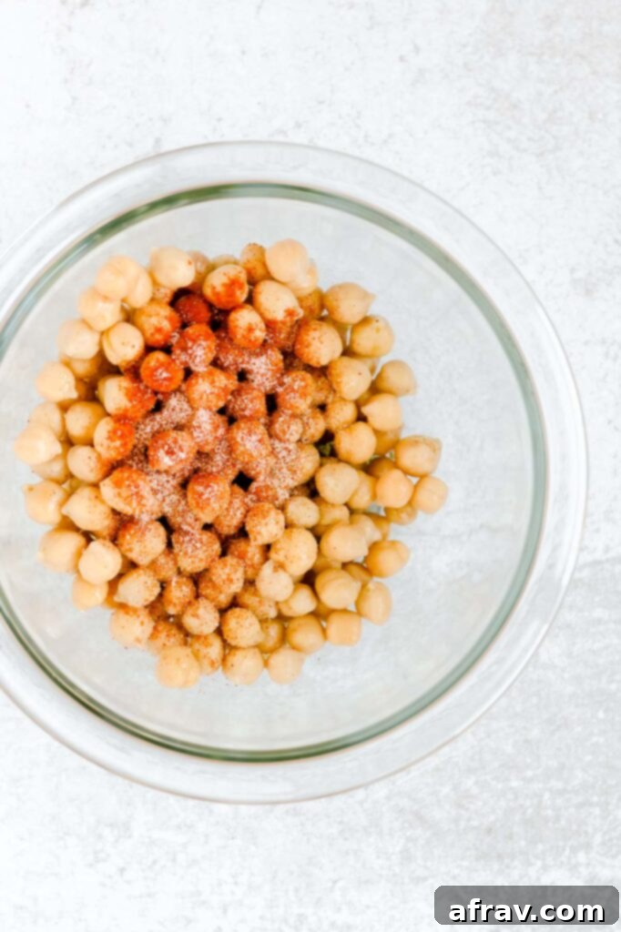 Seasoning sprinkled on chickpeas in a glass mixing bow.
