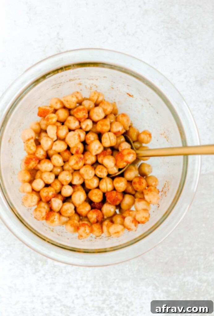 Chickpeas and seasoning mixed together in glass mixing bowl.