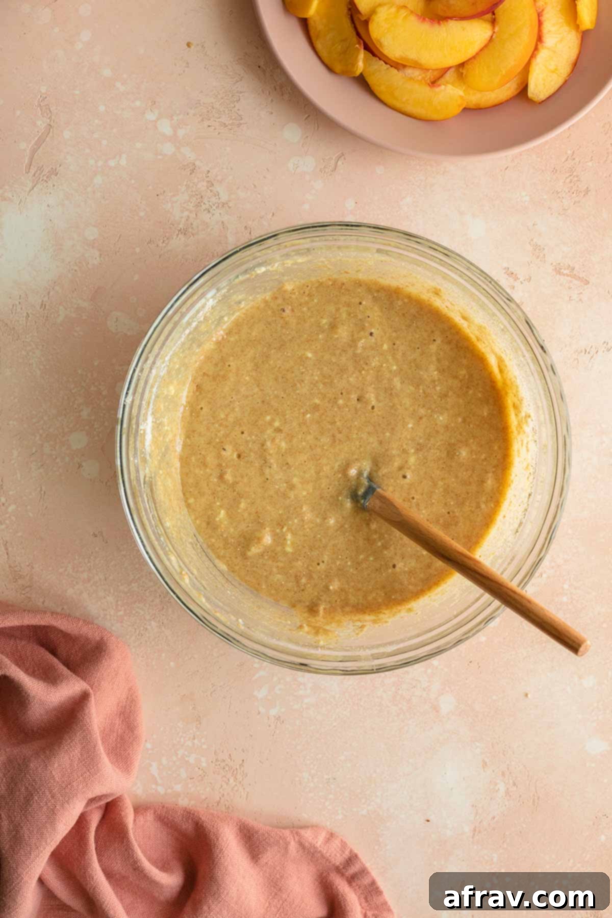 Peach cake batter in a glass bowl with a spatula inserted into it, showing consistency.
