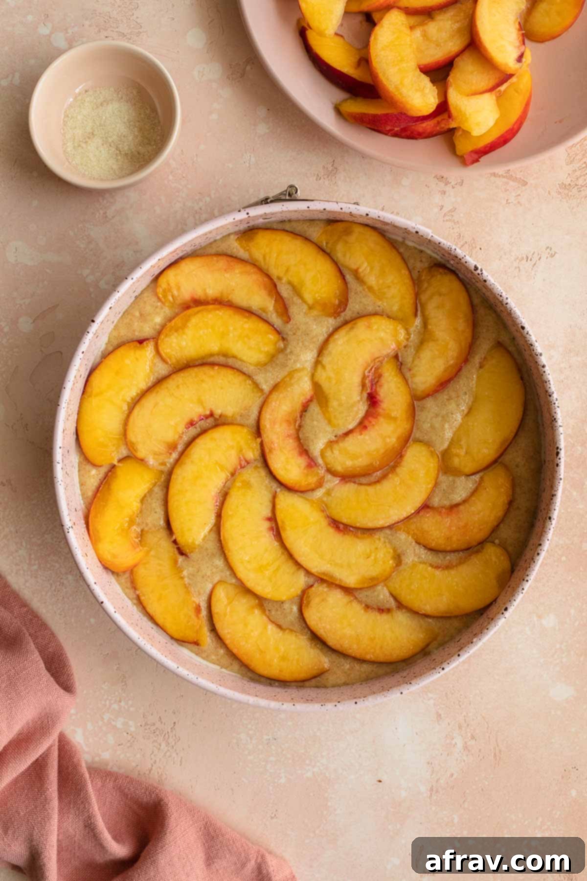 Cake batter in a springform pan, topped artfully with peach slices before baking.