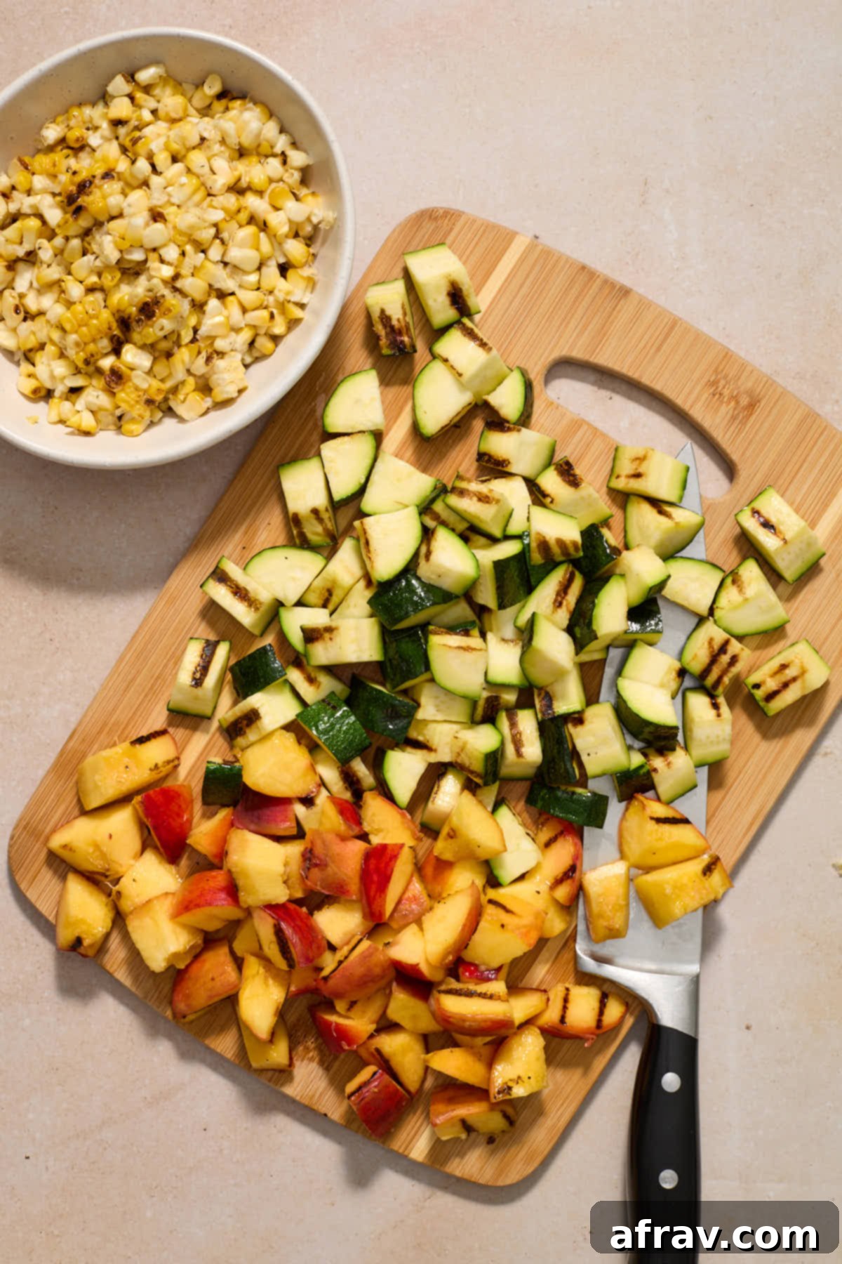 Charred Vegetable and Peach Orzo Summer Salad 8 Chopped zucchini and peaches on a wooden board with a bowl of corn on the side.
