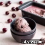 Two scoops of vegan cherry ice cream in a small dark bowl.