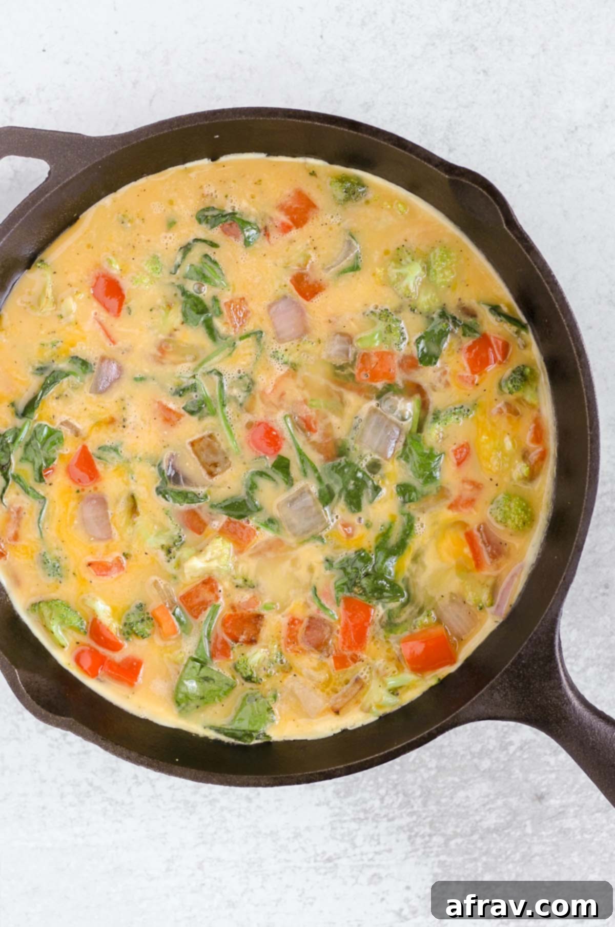 Whisked eggs mixed with veggies in a cast iron skillet.