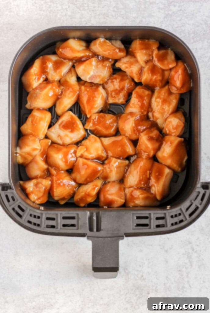 Raw chicken coated with teriyaki sauce in air fryer basket.