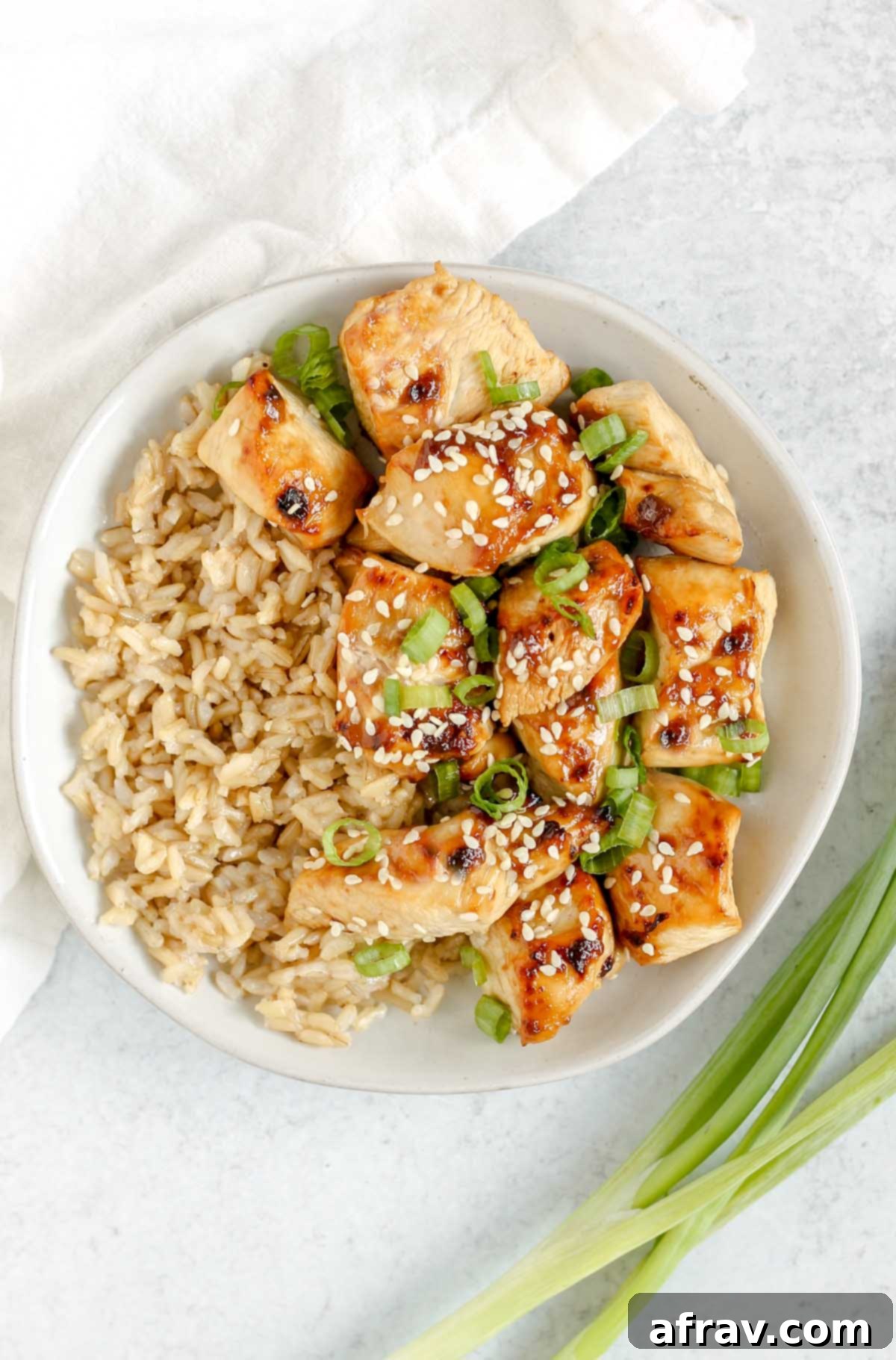 Teriyaki chicken pieces with brown rice on a white plate.