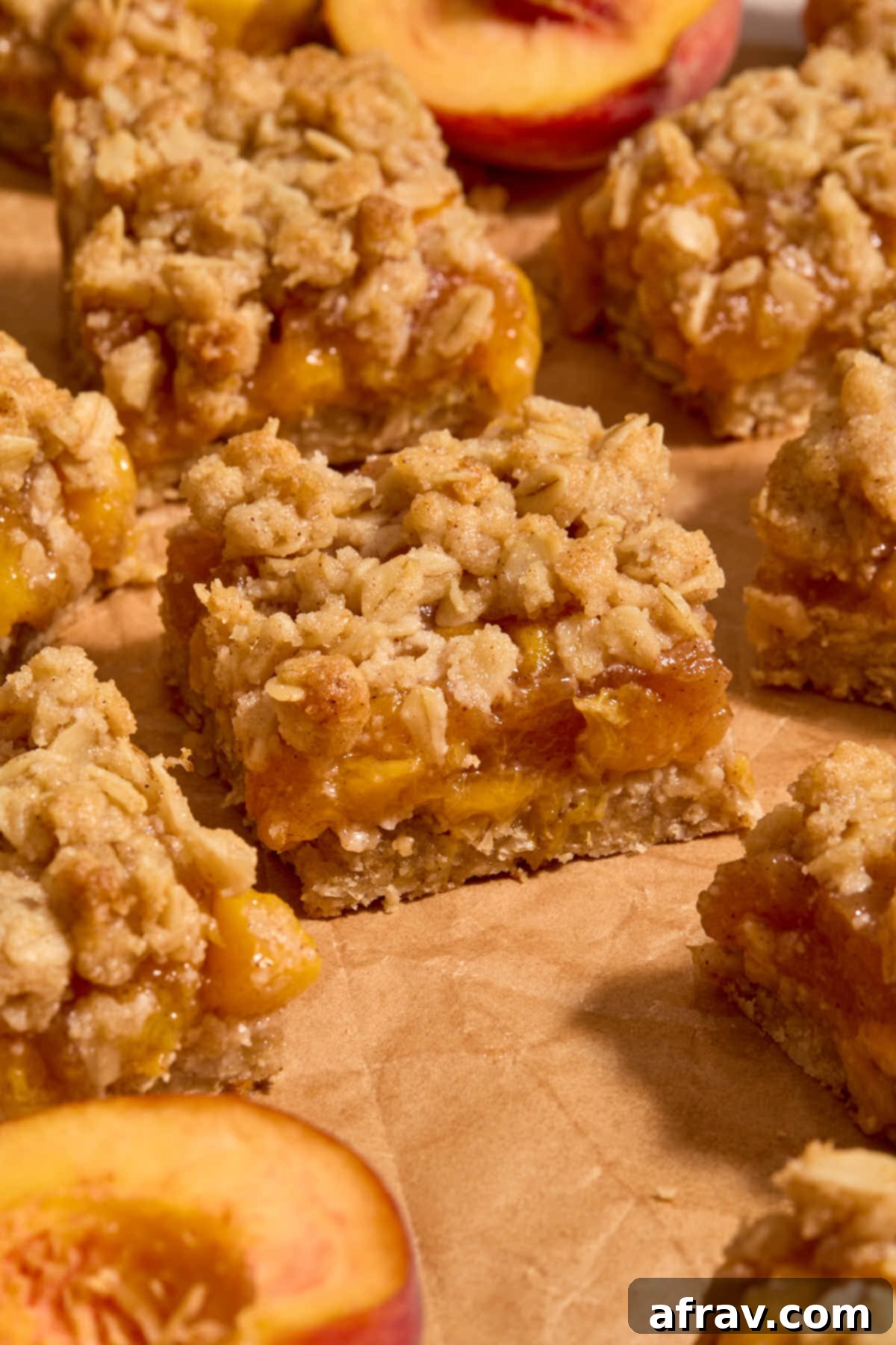 Side view of peach bars arranged on crumpled brown parchment paper with peach halves around them, highlighting the layers.