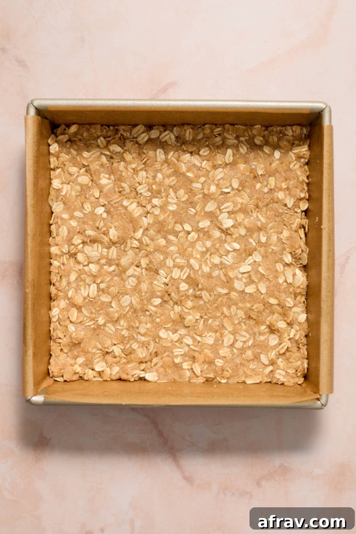 Crust for the peach bars pressed into a parchment lined square pan, creating an even layer.