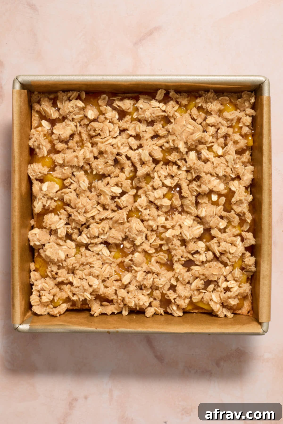 Peach filling and crumble topping layered on top of the crust in a baking pan, ready for the oven.