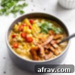 Vegan Corn Chowder with Crispy Coconut Bacon 2 Dairy-free corn chowder in a dark bowl on a light surface with cilantro and coconut bacon in the background.