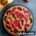 Overhead view of a buttermilk plum cake cooling on a round wire rack on a dark surface.