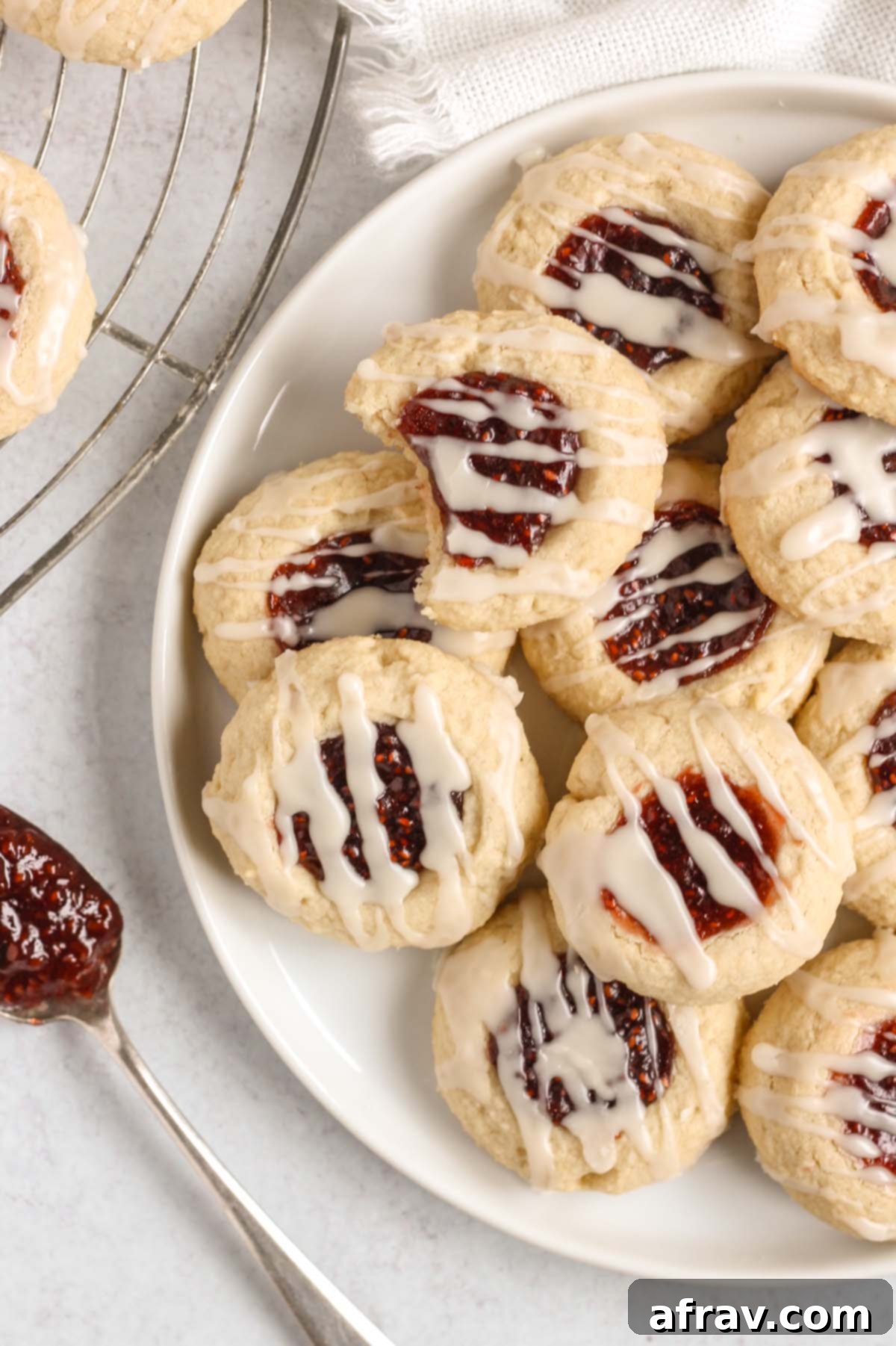 Gluten-free raspberry thumbprint cookies on a white plate, showcasing their perfect shape and vibrant filling.