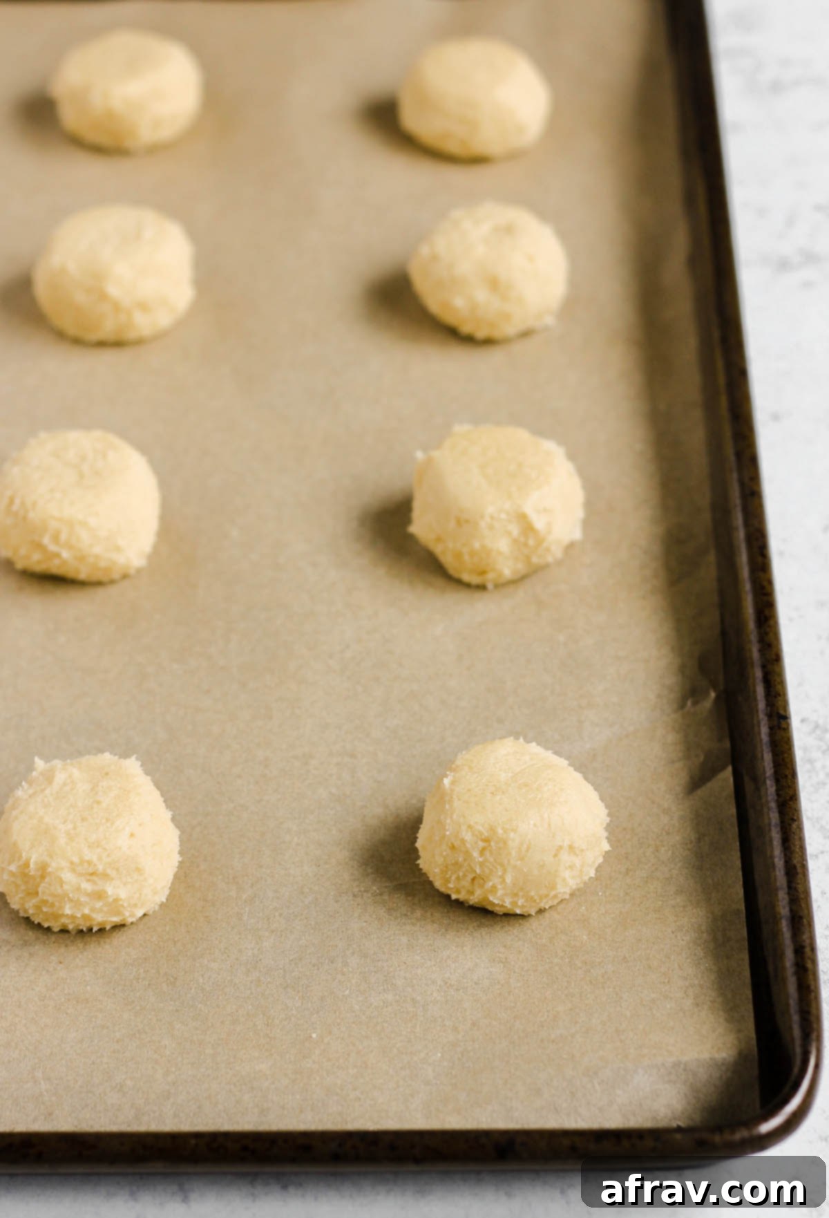 Dough balls neatly arranged on a parchment paper lined cookie sheet, ready for indentation.