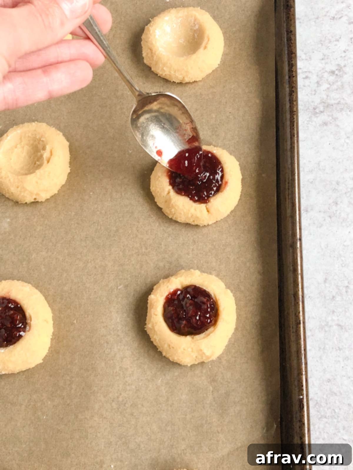 Spoon filling cookies with raspberry jam before baking.