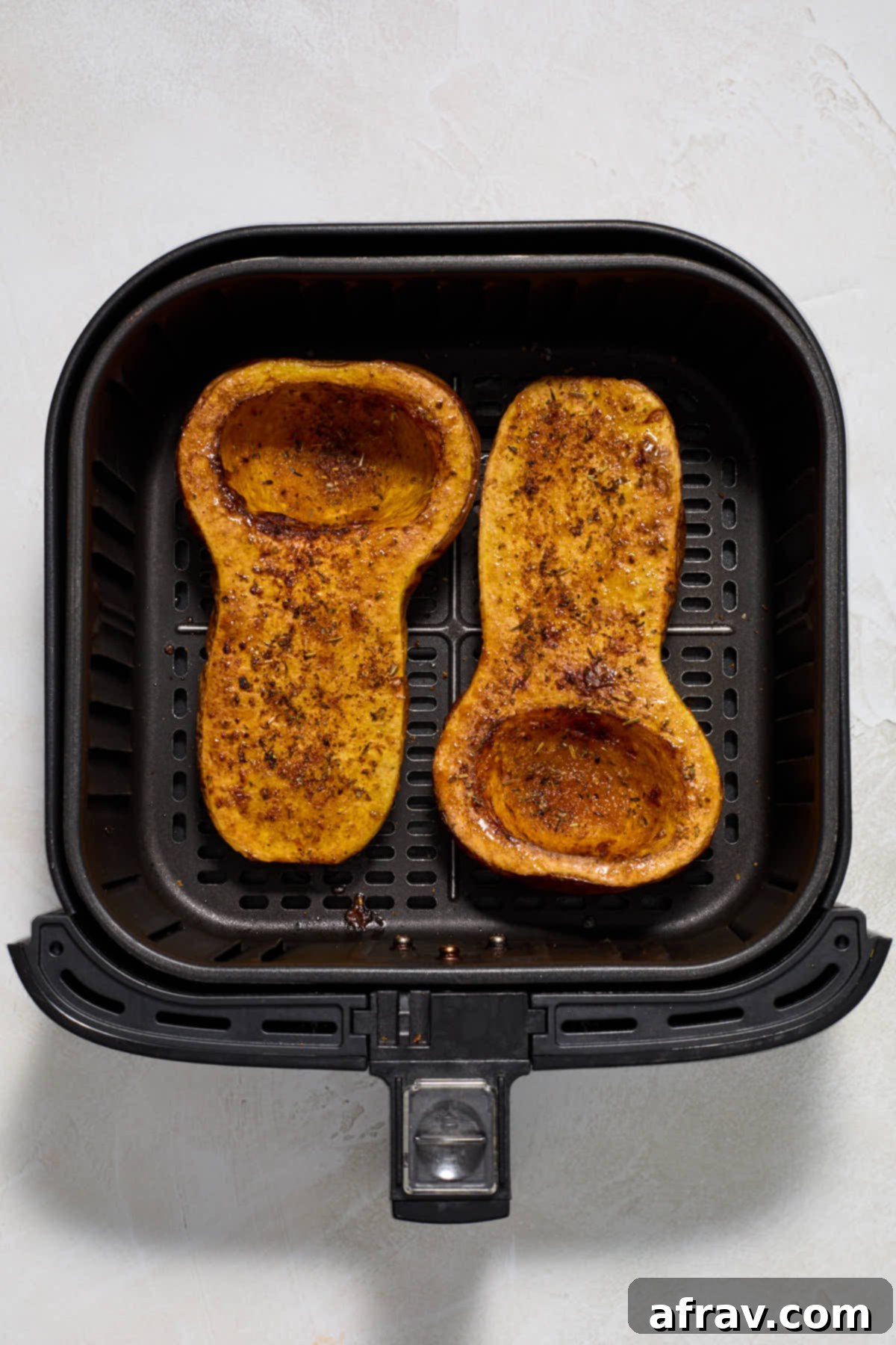 Fully air fried butternut squash halves in an air fryer basket, golden brown and fork-tender.
