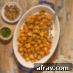 Air fryer butternut squash cubes in a serving dish with chopped pecans, pumpkin seeds and fresh herbs.