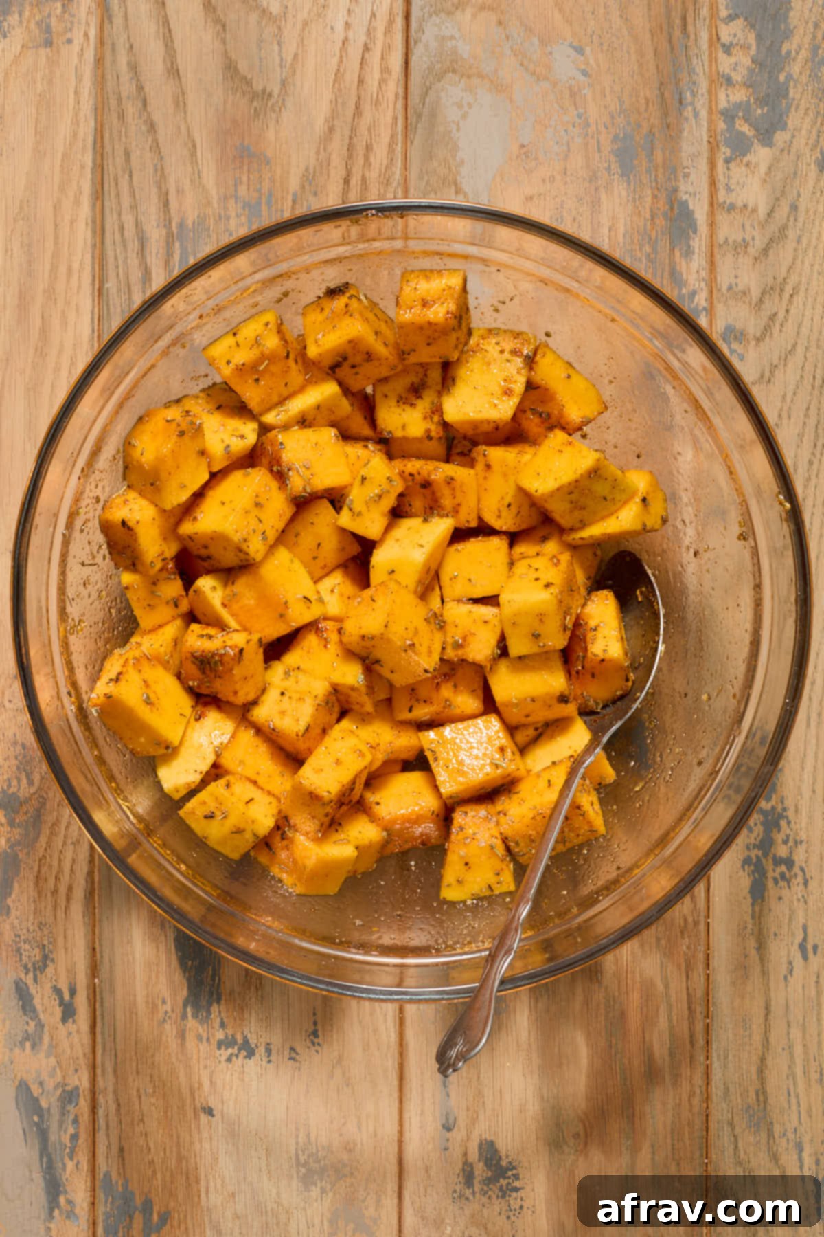 Butternut squash cubes seasoned with Italian seasoning, dried sage, garlic powder, smoked paprika, and salt in a glass bowl.