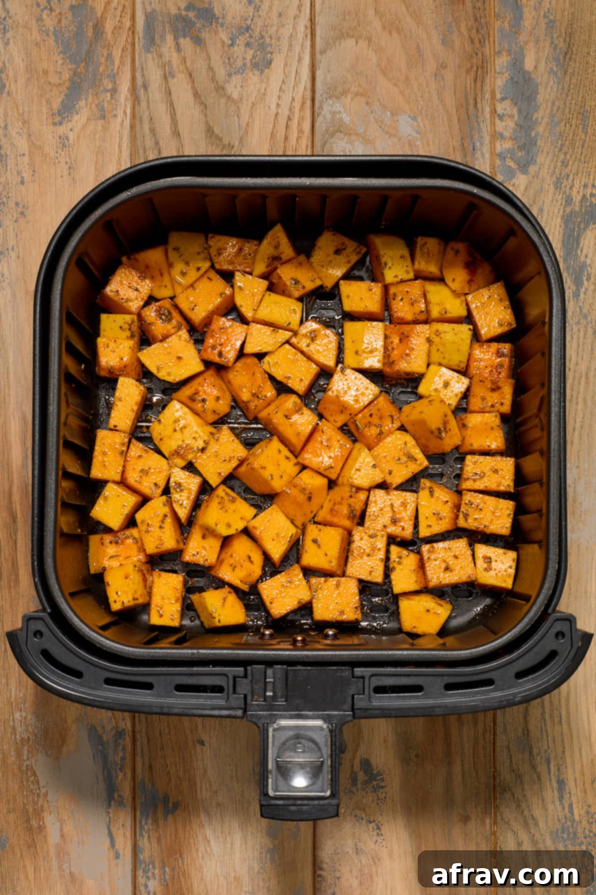 Seasoned butternut squash cubes arranged in a single layer within an air fryer basket, ready for cooking.