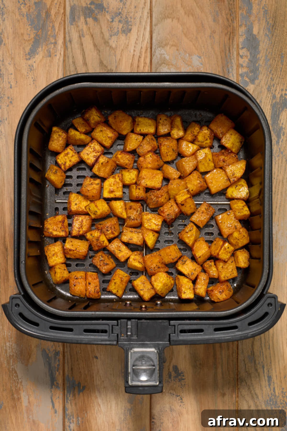 Golden brown and tender air fried butternut squash cubes in an air fryer basket after cooking.