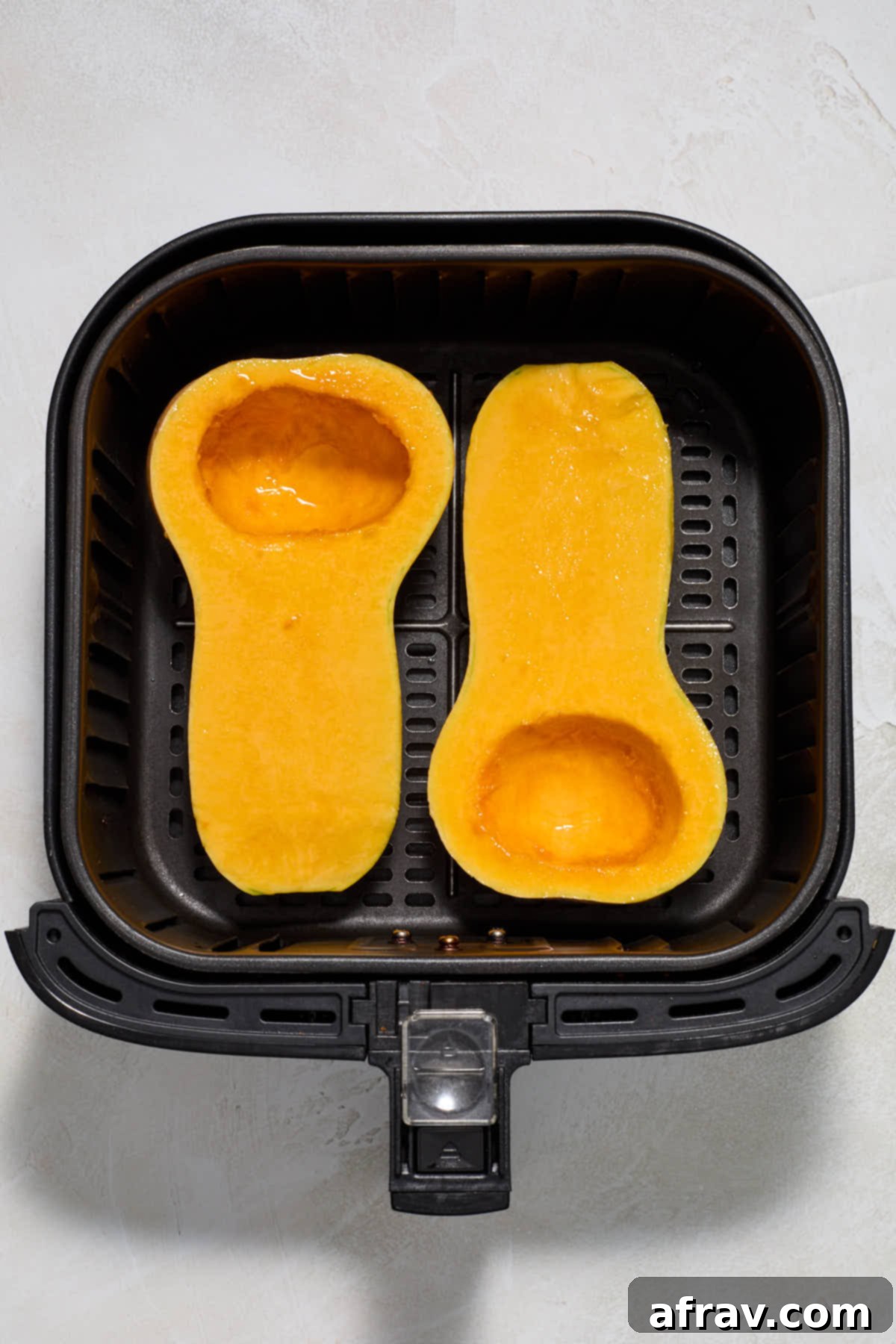 Butternut squash halves, cut lengthwise, with the flesh brushed with olive oil and arranged cut-side-up in an air fryer basket.