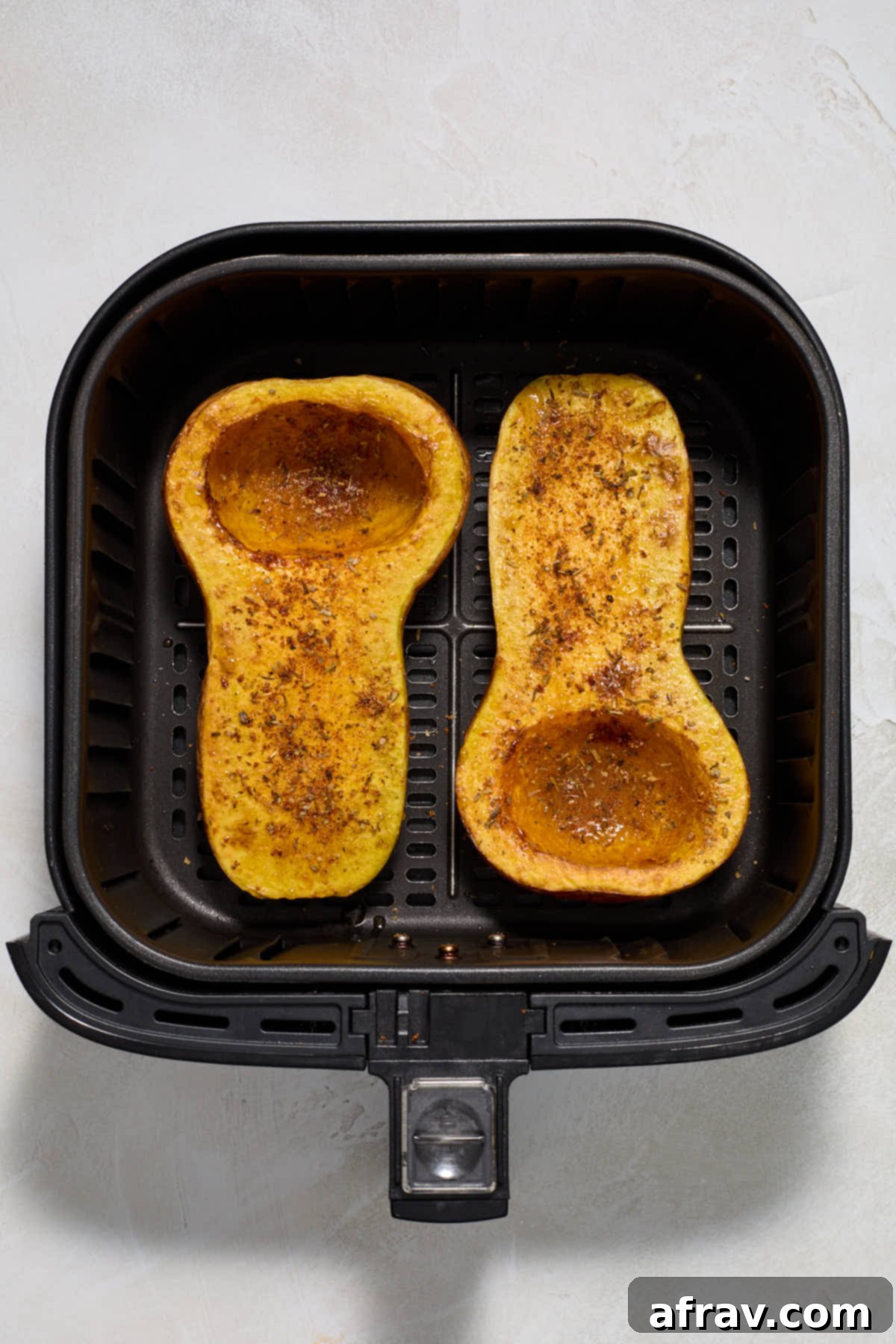Butternut squash halves after partial air frying, now brushed with maple syrup and sprinkled with a blend of seasonings.