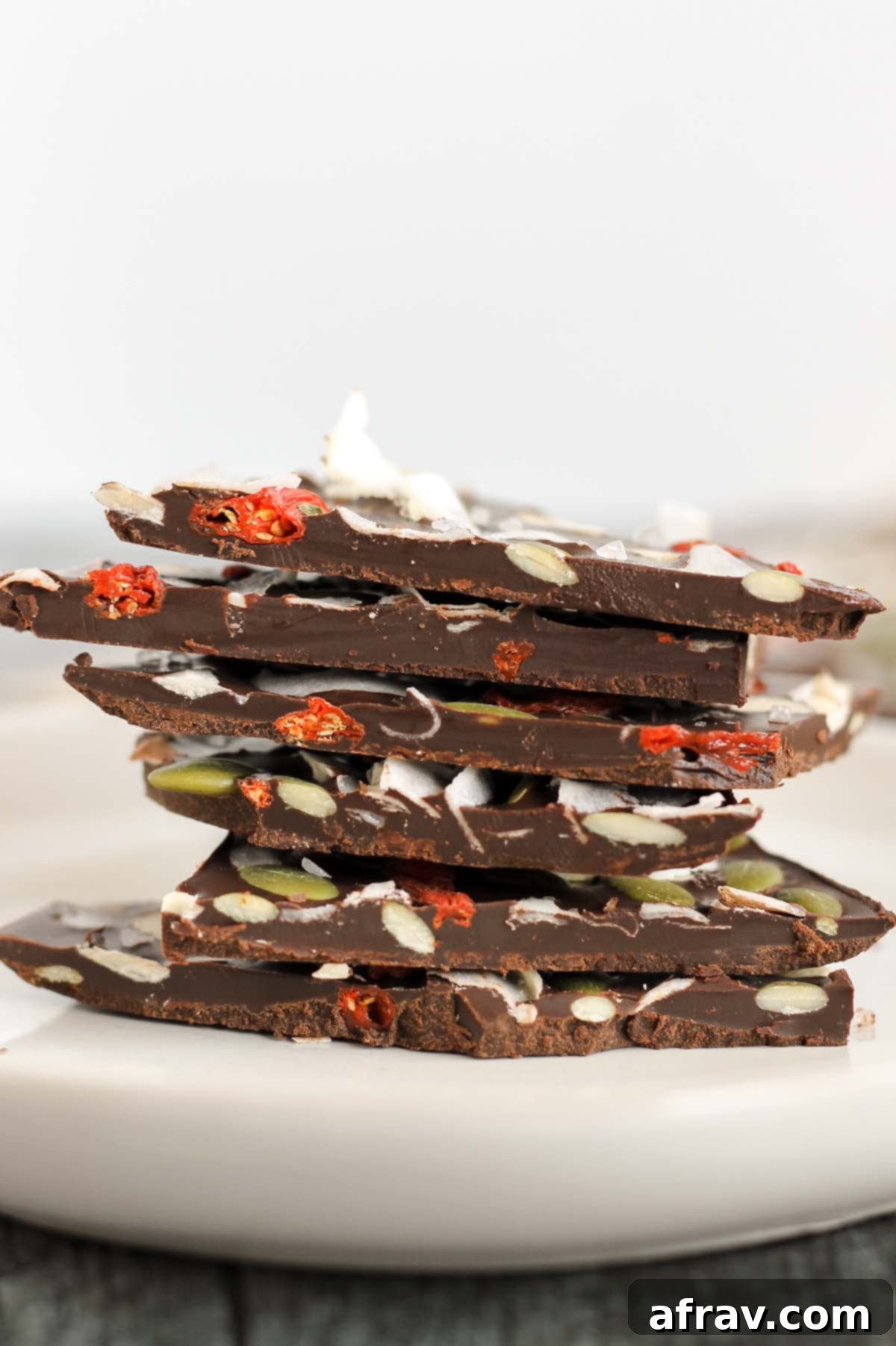 Stacked pieces of healthy dark chocolate bark, showcasing its rich texture and colorful toppings like goji berries, pumpkin seeds, and almonds.