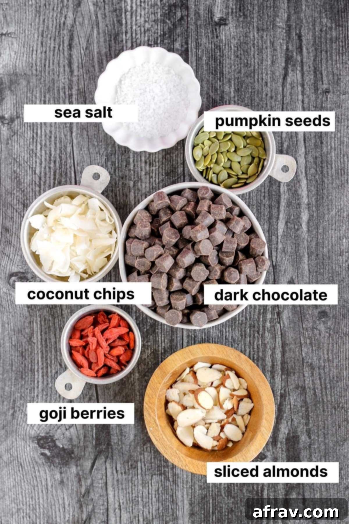 Labeled ingredients for healthy dark chocolate bark, including dark chocolate gems, goji berries, pumpkin seeds, almonds, coconut flakes, and sea salt.