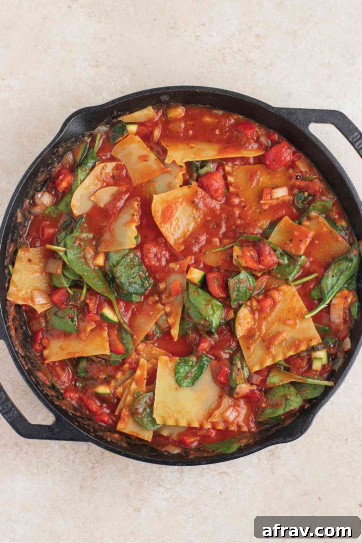 Uncooked vegetarian lasagna ingredients in a cast iron skillet, with noodles covered in sauce.