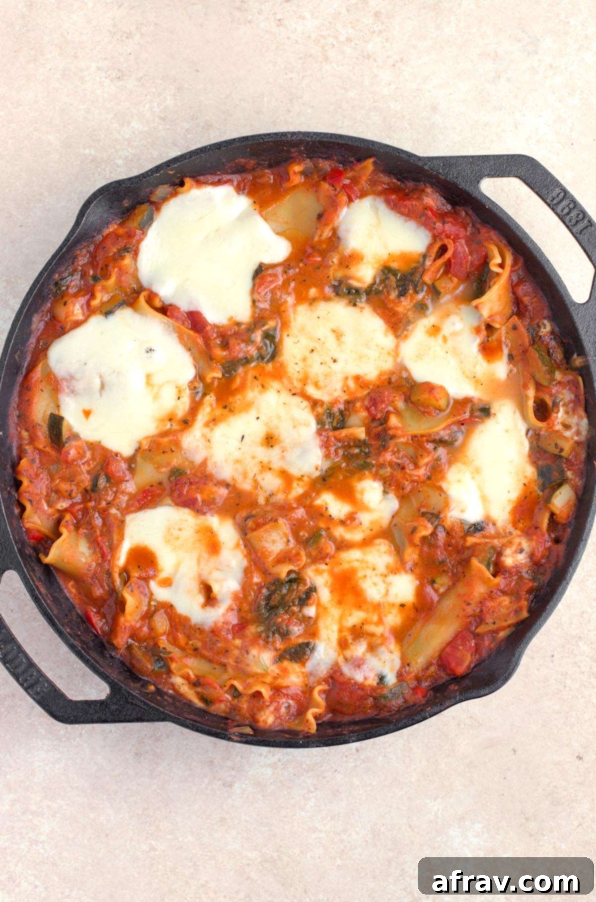 Cooked vegetable lasagna in cast iron skillet, bubbling and ready for cheese.
