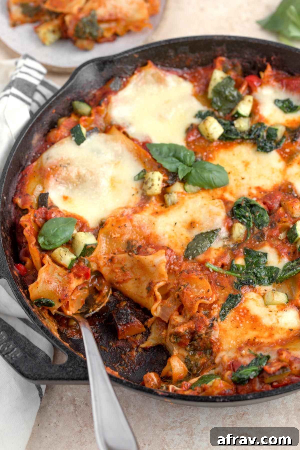 A spoon scooping vegetable lasagna skillet out of a cast iron skillet, showing layers of noodles, sauce, and cheese.