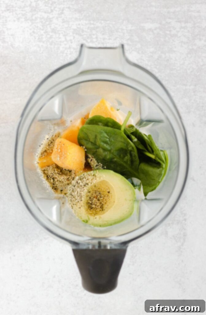 Avocado, mango, spinach, hemp seeds, and milk loaded into a blender cup, ready for blending.