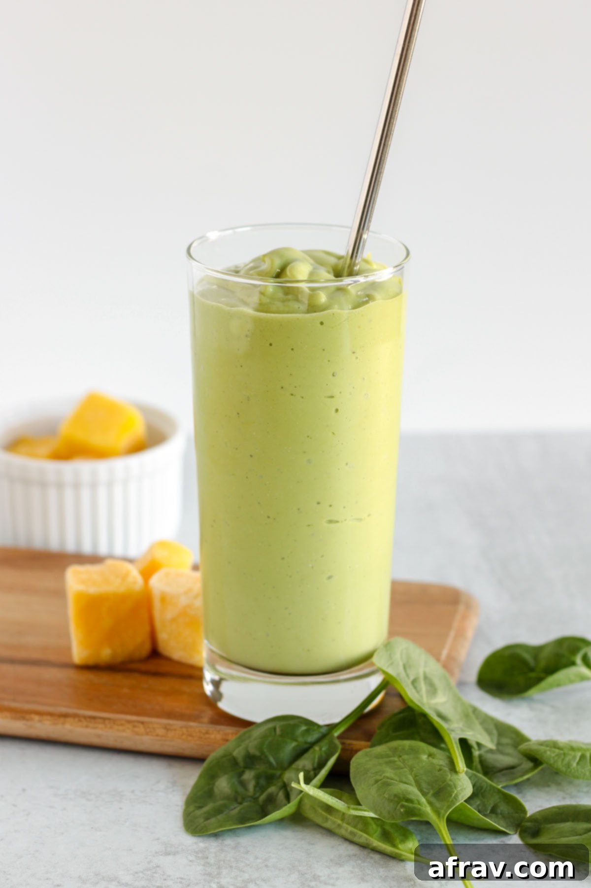 Tall glass filled with a vibrant green spinach mango smoothie, garnished with a stainless steel straw, ready to be enjoyed.