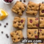 Overhead view of cranberry chocolate chip cookies cut into squares next to fresh cranberries and chocolate chips.