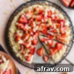 Overhead view of strawberry custard tart on a round wire rack with a piece removed.
