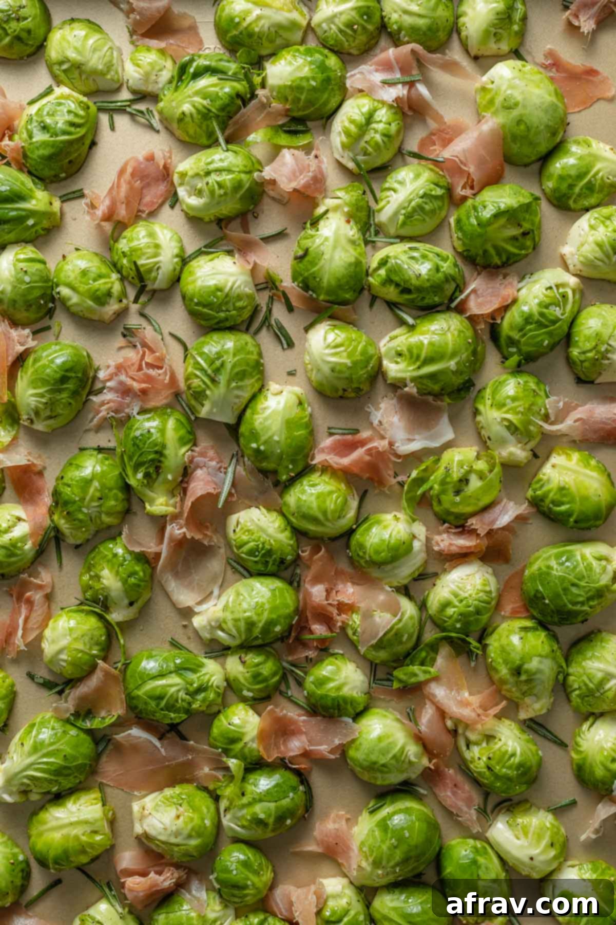 Brussels sprouts and prosciutto arranged in a single layer on a baking sheet before roasting.