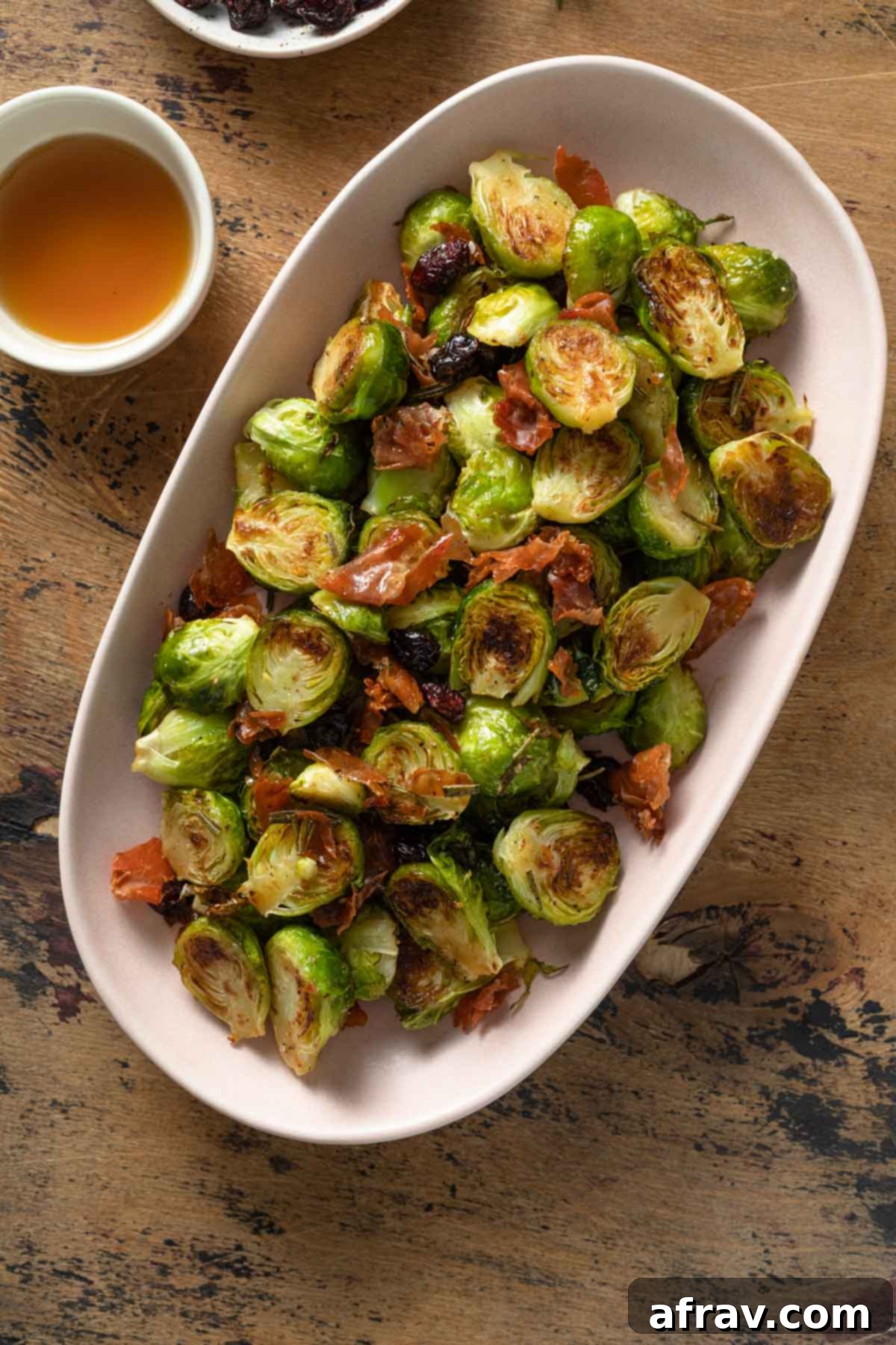 Prosciutto Brussels sprouts tossed with maple syrup and dried cranberries in a white serving dish.