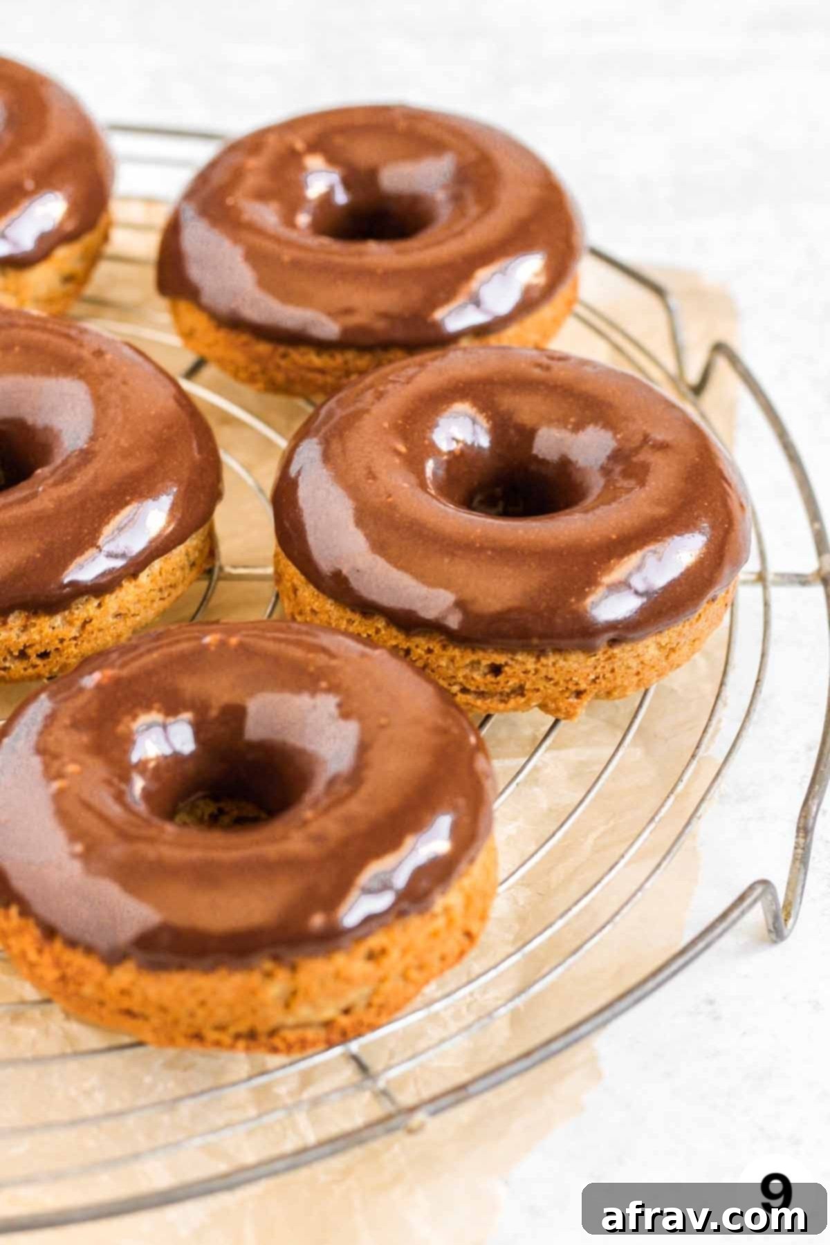 Chocolate frosted donuts on a round wire cooling rack.