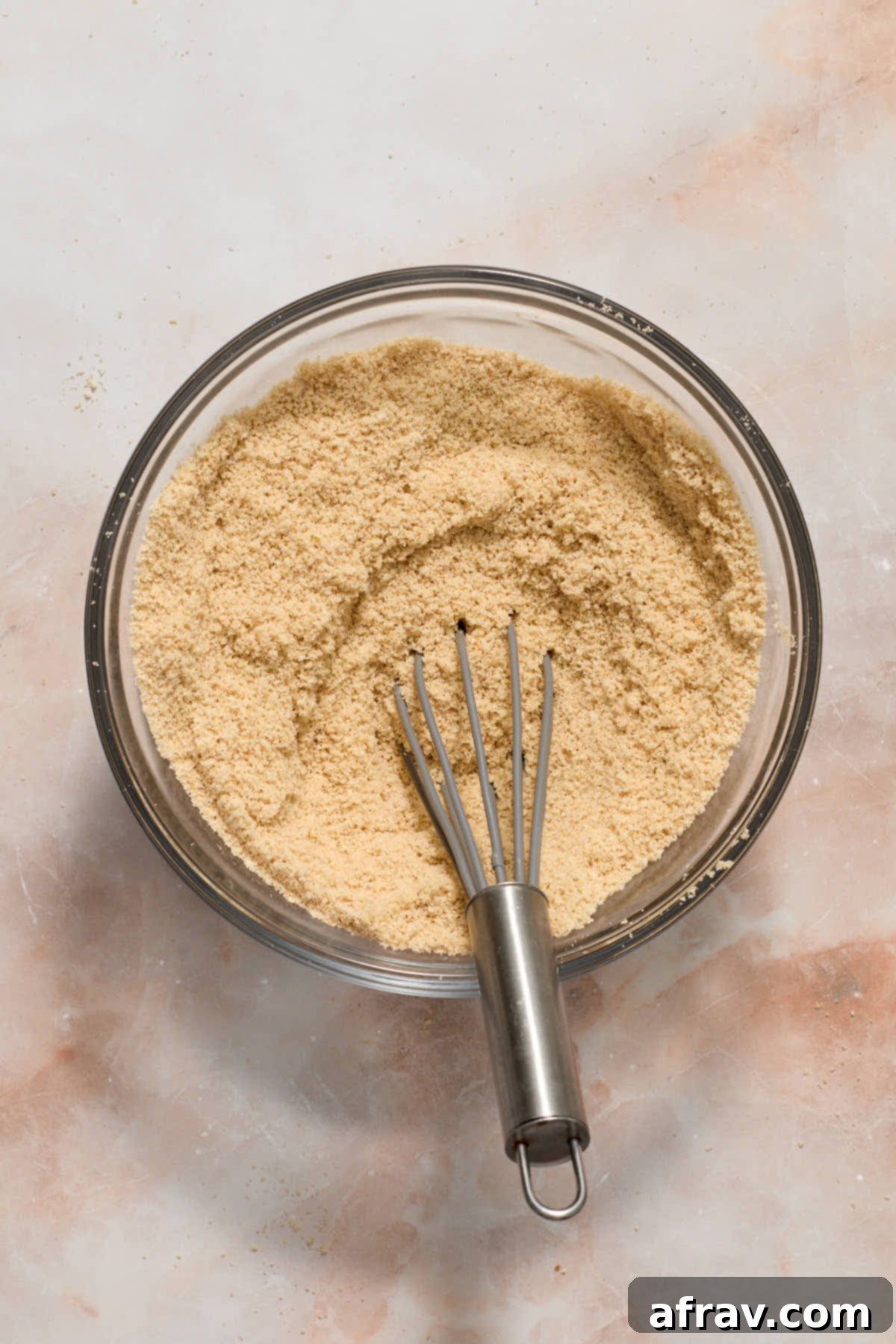 Dry ingredients like almond flour, cornstarch, and spices whisked together in a clear glass bowl.